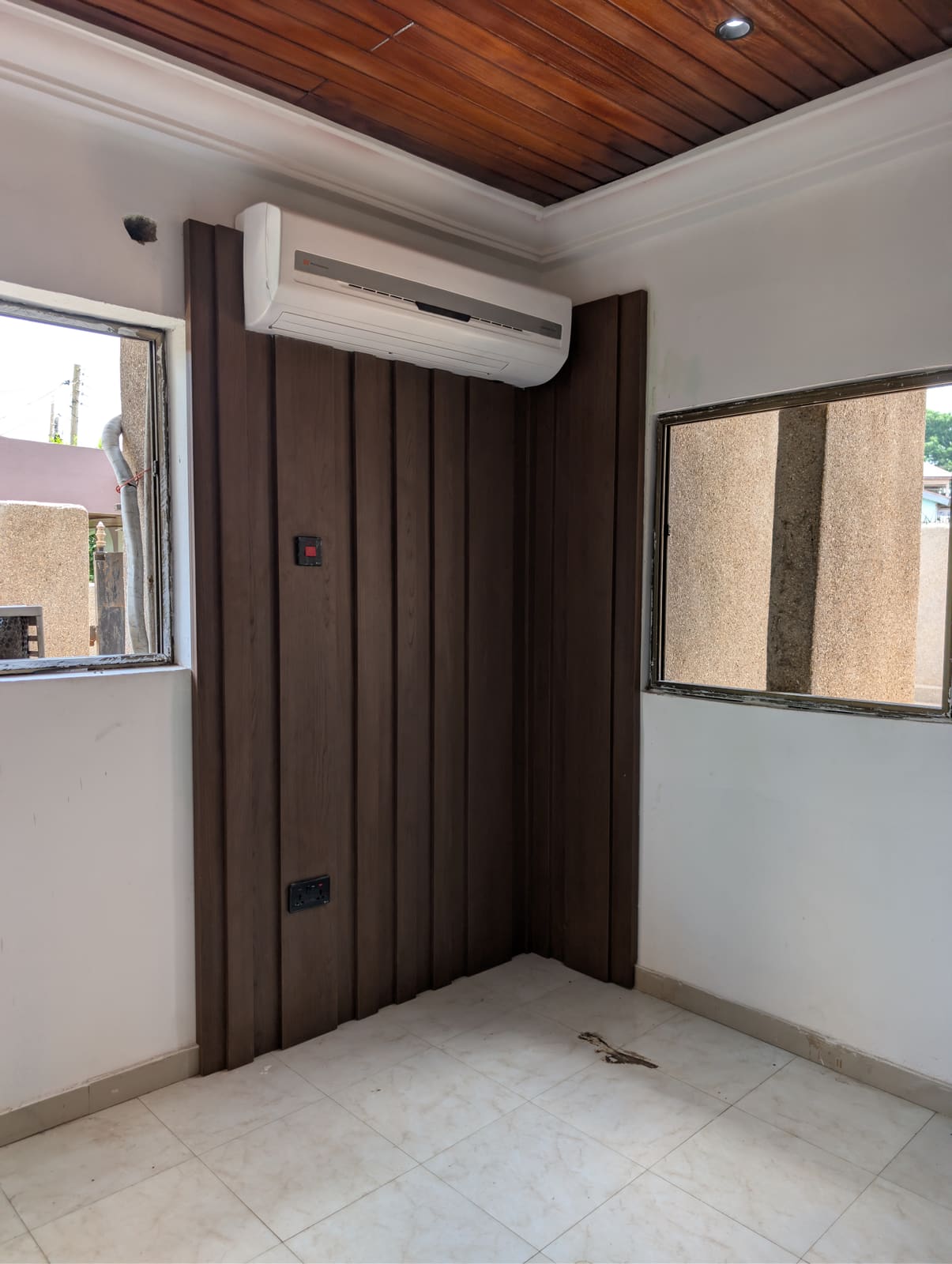 Walnut-toned slat wall paneling around the air-conditioning unit, Achimota guesthouse