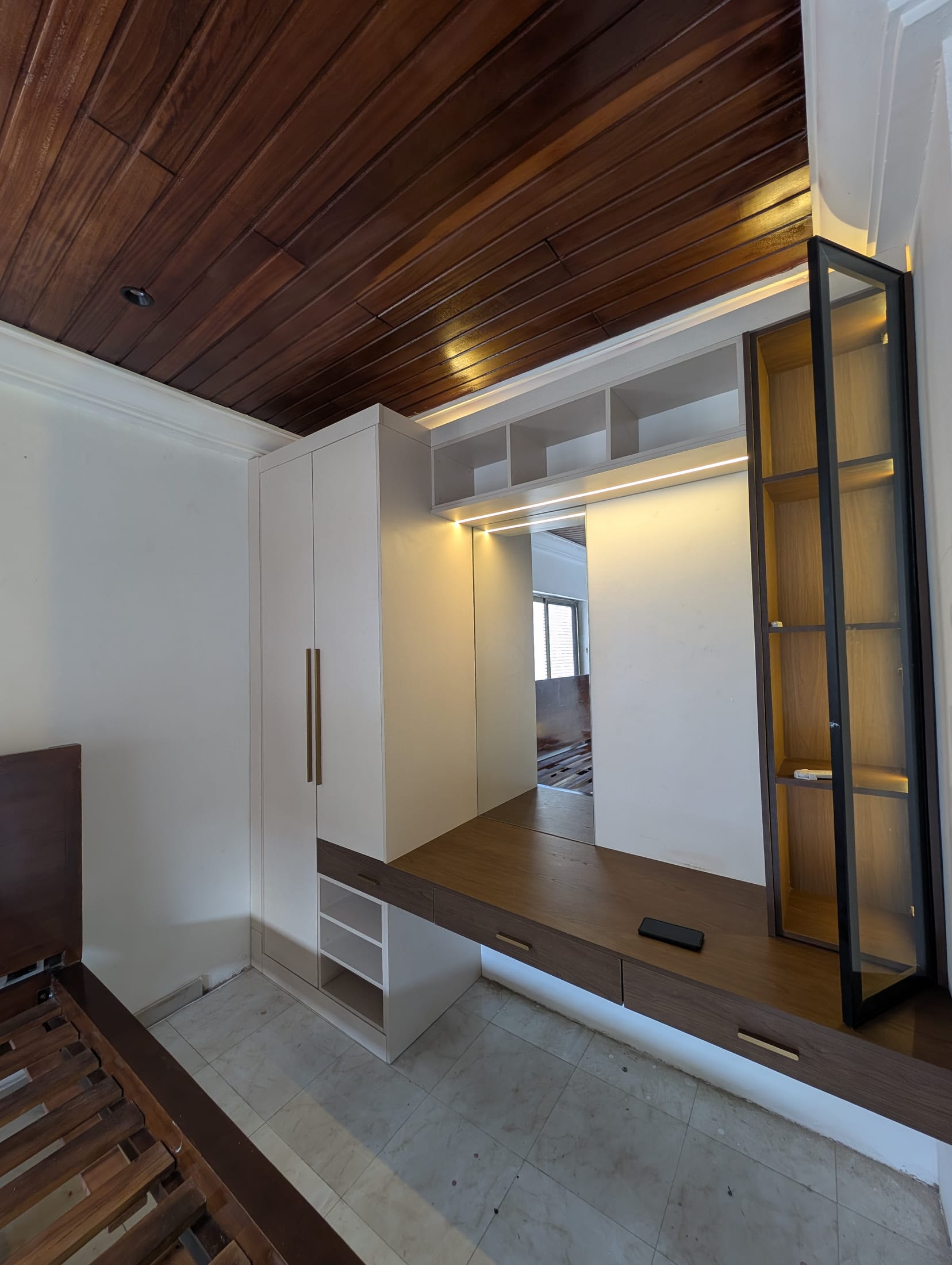 Guesthouse room conversion in Achimota, Accra — built-in wardrobe, floating vanity, and lit glass display cabinet under a wood-slat ceiling, built by Neewoody Custom Woodwork