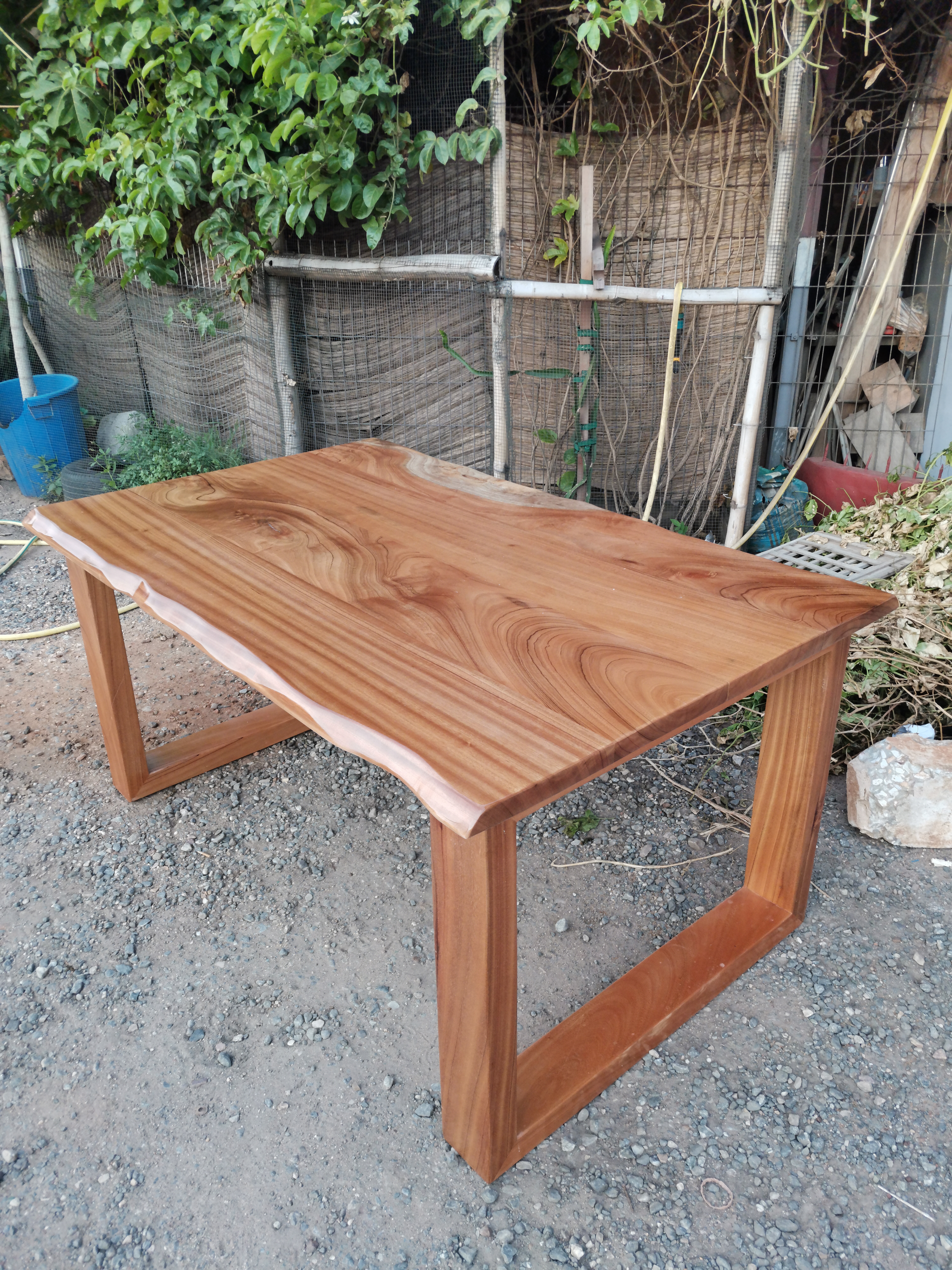 Afromosia live-edge dining table photographed outdoors before delivery — natural grain and live edge visible